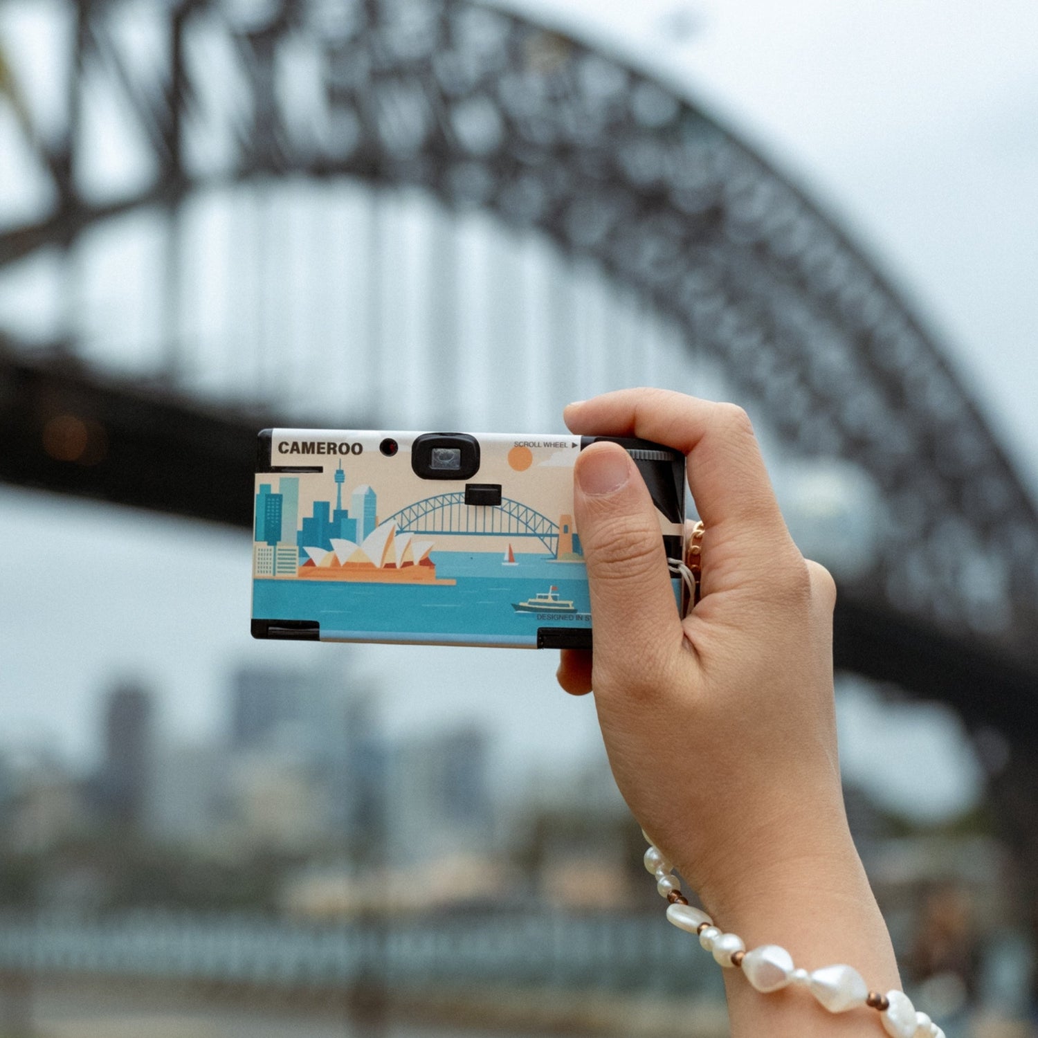 Cameroo disposable camera with Sydney Harbour illustration held up in front of the Sydney Harbour Bridge