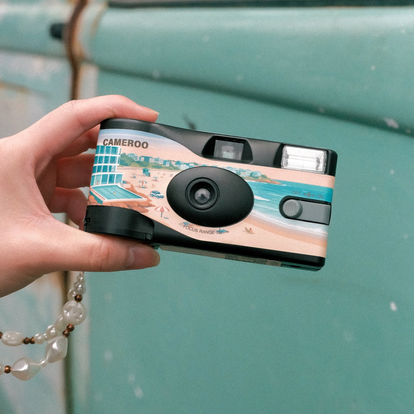 Cameroo Aussie Summer disposable camera front view held in hand, beach view, bondi beach, real product photo